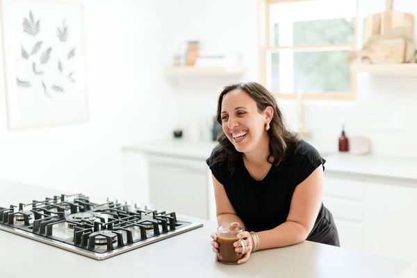 Soof laughing in her kitchen holding a coffee